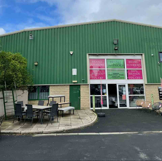 Green industrial Brand Interiors Colne Store building with large windows and outdoor seating area outside store
